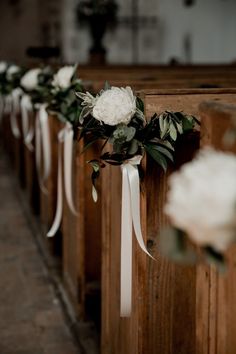 white flowers and greenery are tied to the pews