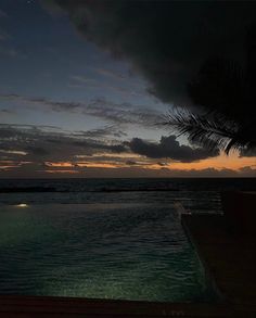 an empty swimming pool at night with the sun setting in the distance and clouds above