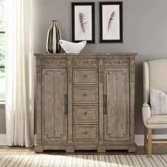 a white chair sitting next to a wooden cabinet in a room with two pictures on the wall