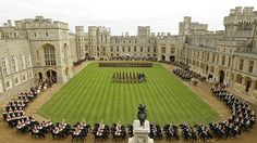 a group of people standing in front of a large building with a lawn and horse drawn carriages