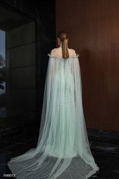 a woman in a white dress with a long veil on her head is standing against a wall