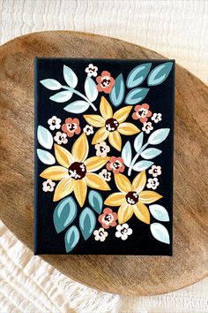 a wooden table topped with a black box covered in colorful painted flowers and leaves on top of it