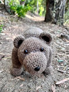 a crocheted teddy bear sitting on top of a dirt road in the woods