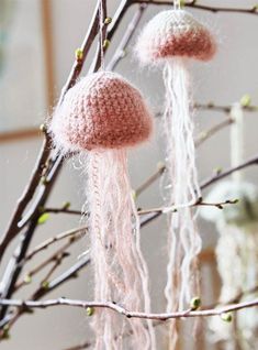 two pink knitted mushrooms hanging from a tree branch with the caption saying,