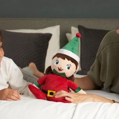 a woman laying in bed next to a child with an elf doll on her lap