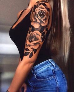 a woman with long hair wearing a black shirt and blue jeans, has a rose tattoo on her arm