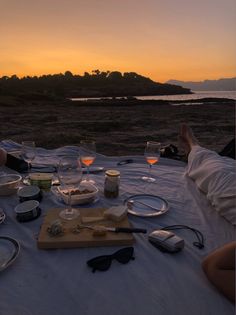 two people sitting at a table with food and drinks in front of an ocean sunset