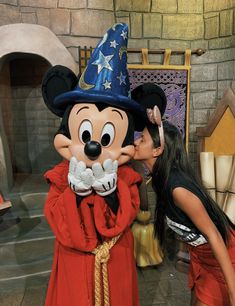 a woman kissing mickey mouse in front of a castle