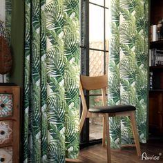 a wooden chair sitting in front of a window covered in green leafy curtain panels