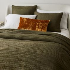 a bed with green bedspread and brown pillows