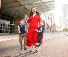 a woman in a red dress is walking with two small boys and holding hands up