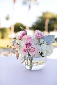 a vase filled with flowers on top of a white table cloth covered tablecloth in front of palm trees