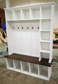 a large white bookcase with several shelves and hooks on the wall, in a room under construction