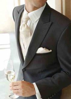 a man in a tuxedo holding a glass of wine and looking at the camera