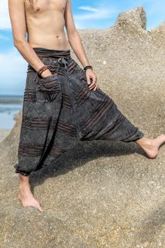 a shirtless man standing on top of a rock near the ocean with his hands in his pockets