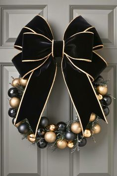 a wreath with black and gold ornaments hanging on the front door, decorated with a bow