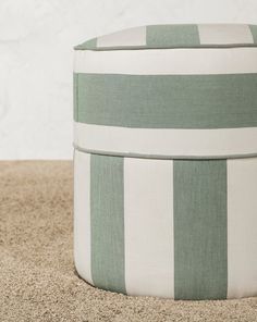 a green and white striped ottoman sitting on top of a carpeted floor next to a wall