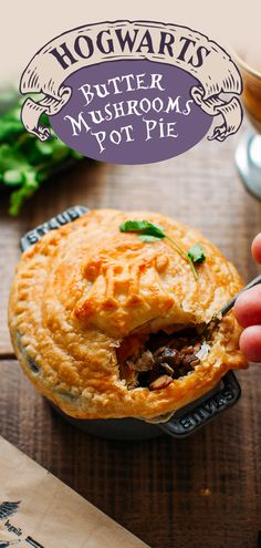 a hand holding a piece of food over a pot pie on top of a wooden table