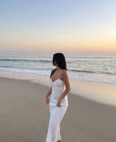 a woman standing on top of a sandy beach next to the ocean in white dress