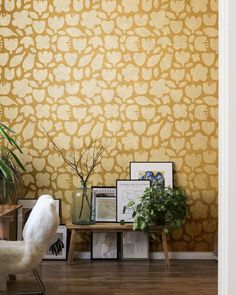 a white chair sitting in front of a wall covered in yellow stone pattern paint next to a potted plant