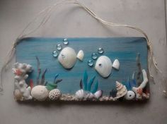 a wooden sign with sea shells and other marine life on the bottom, hanging from a rope