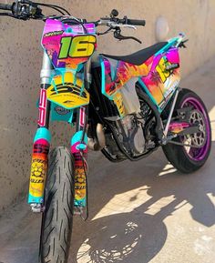 a colorful dirt bike parked next to a wall with graffiti on it's side