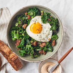 an egg is on top of some greens in a bowl with bread next to it