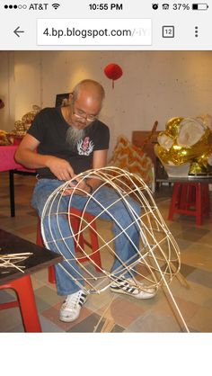 a man sitting on top of a red chair next to a wire sculpture