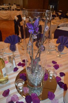 a vase filled with purple flowers on top of a white and purple table cloth covered table