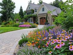 a house with lots of flowers in the front yard and walkway leading to it's entrance