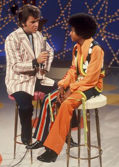 two men sitting on stools talking to each other