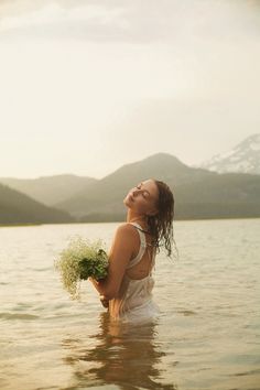 a woman is standing in the water with her eyes closed and holding some flowers to her chest