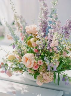 a vase filled with lots of flowers sitting on top of a white table covered in greenery