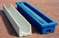 two blue plastic troughs sitting on top of a gravel ground next to each other