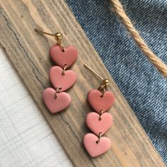 three heart shaped earrings hanging from hooks on a piece of wood next to a pair of jeans