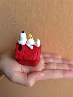 a hand is holding a small red box with two white dogs on it and one black nose