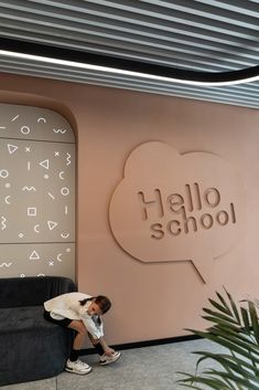 a person sitting on a couch in front of a wall with the words hello school