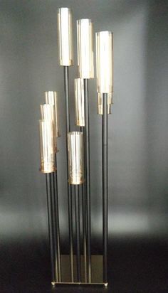 a tall metal and glass sculpture with five candles on it's base in front of a black wall