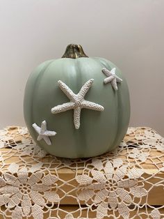 a green pumpkin decorated with starfish on top of a lace doily table cloth