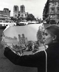 a woman holding up a large painting in the middle of a street