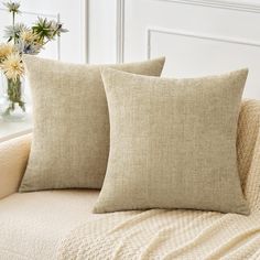 two pillows sitting on top of a couch next to a vase with flowers