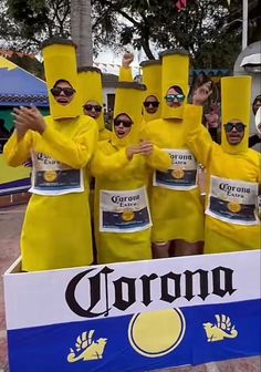 a group of people in yellow outfits standing next to a corona sign with their hands up