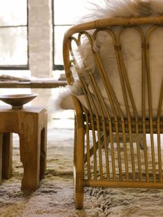 a wicker chair with white cushions in front of a window and table next to it