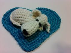 a crocheted white dog laying on top of a blue heart