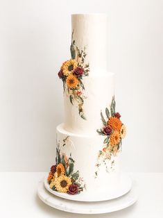 a three tiered wedding cake with flowers painted on the top and bottom, sitting on a white plate