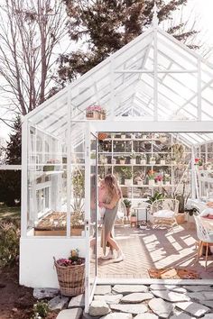 a woman standing in the doorway of a white greenhouse with plants and potted plants