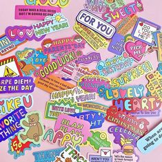 a pile of colorful stickers on top of a pink surface with words written in different languages