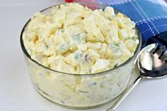 a glass bowl filled with potato salad next to a spoon