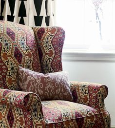 a chair sitting in front of a window next to a vase with flowers on it