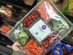 a person holding up a plastic container filled with carrots and broccoli